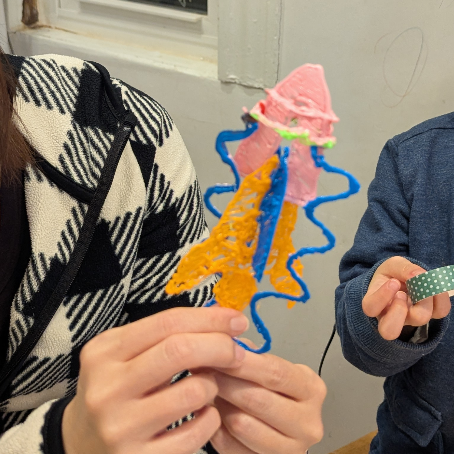 Hands holding completed 3D pen rocket at workshop
